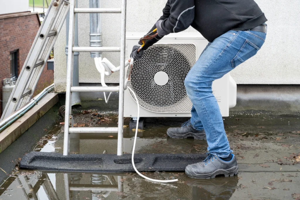HVAC technician servicing an outdoor condenser unit with a hose during a maintenance call
