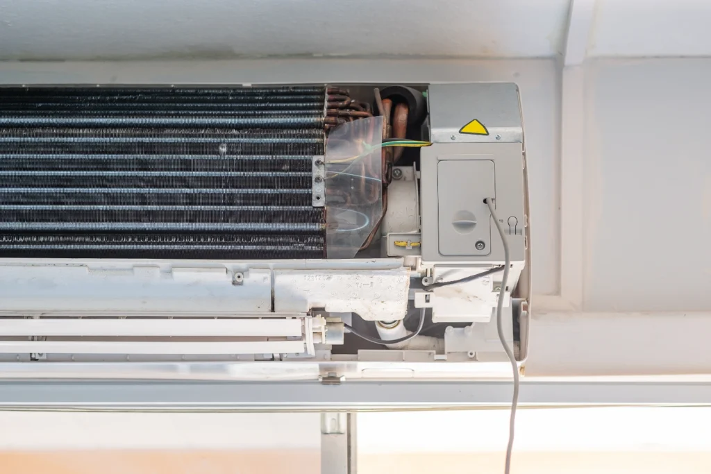 Indoor split system unit opened for service showing the evaporator coil, copper refrigerant lines and control box