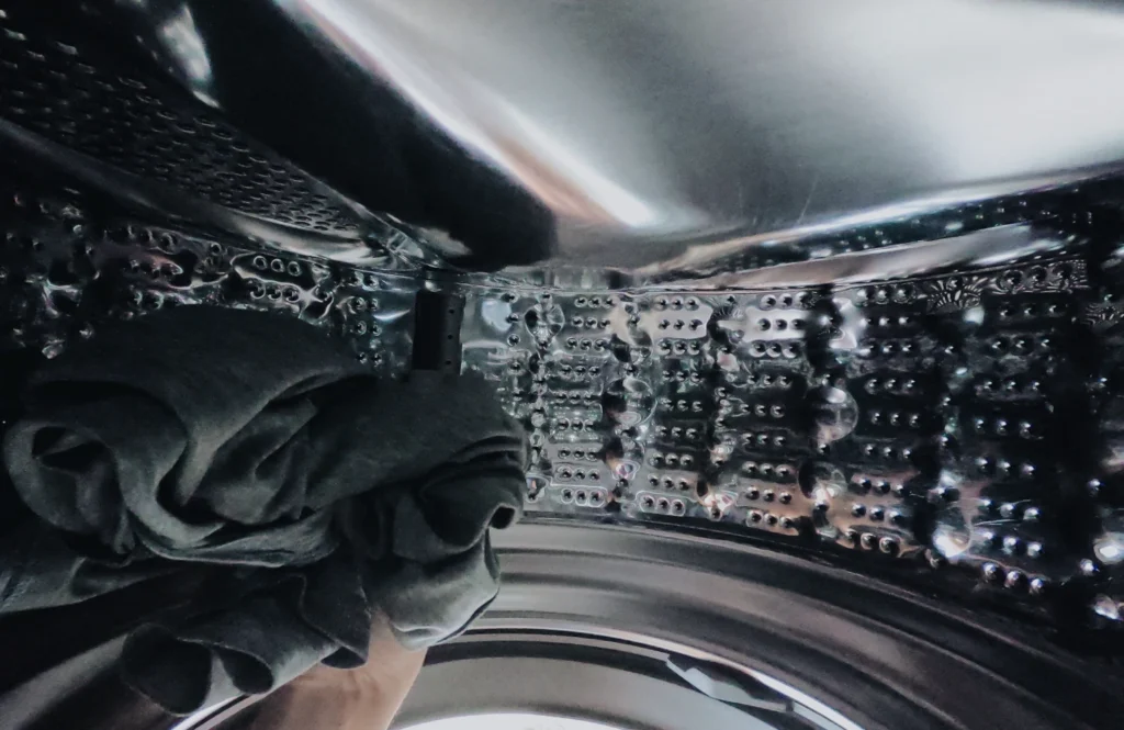 Interior of a stainless washing machine drum holding wet laundry after a cycle failed to drain or spin
