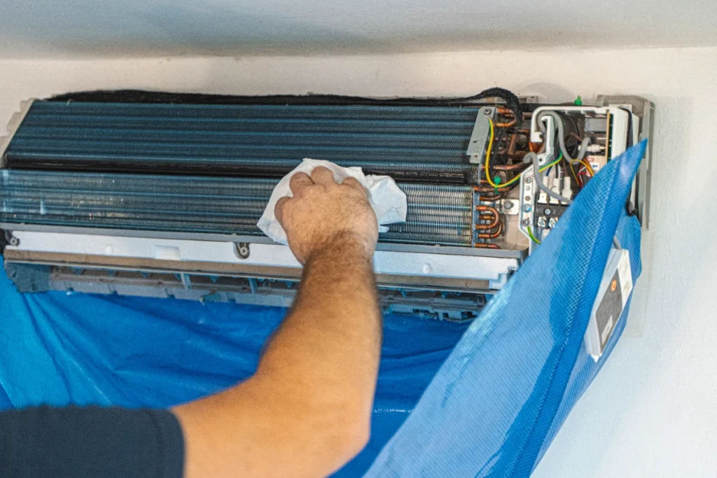 Hand wiping dust from the evaporator coil fins of an open indoor AC unit