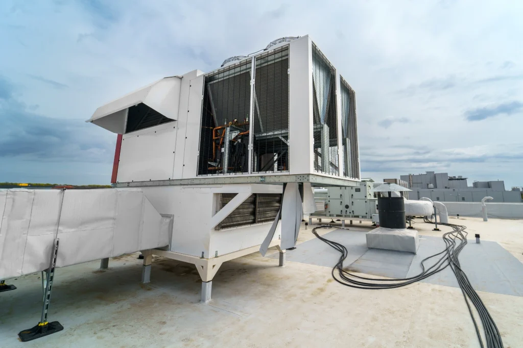 Rooftop packaged HVAC unit with air-cooled condenser fans and insulated supply duct on a flat commercial roof.